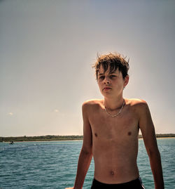 Portrait of shirtless boy standing in sea against sky