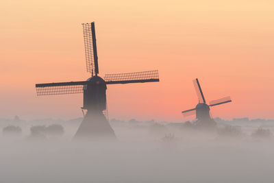 Traditional windmill on landscape against sky during sunset