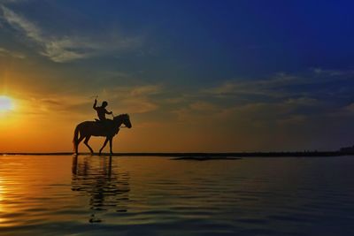 Silhouette man in sea against sky during sunset