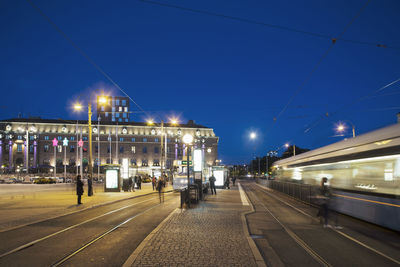 Blurred motion of cable car on illuminated city street against clear blue sky at dusk