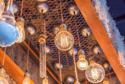 Low angle view of illuminated light bulb hanging from ceiling