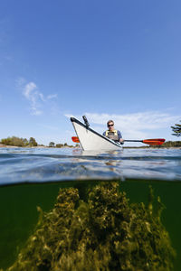 Man sitting on boat against blue sky