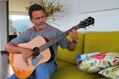 Man playing guitar while sitting on sofa at home