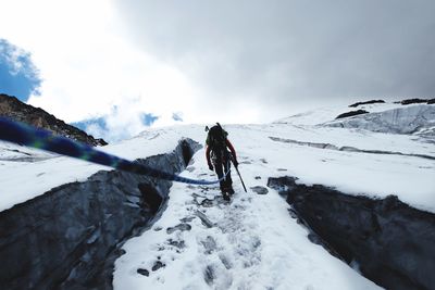 Rear view of man walking on snowcapped mountain during winter