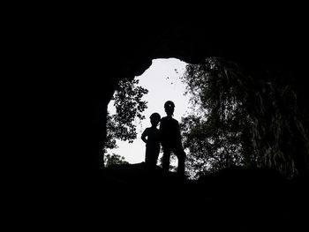 Silhouette people standing on rock against sky