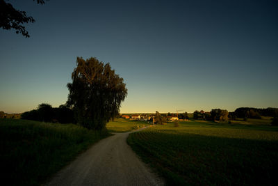 Road amidst field against clear sky