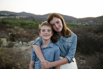 Portrait of loving siblings standing on field during sunset