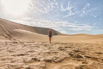 Rear view full length of woman walking at desert against sky on sunny day