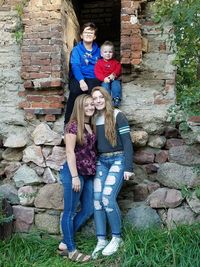 Full length portrait of smiling girl standing against stone wall