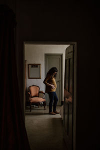 Full length of pregnant woman seen through door at home