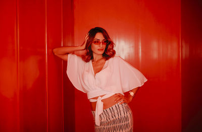 Young woman standing against red wall