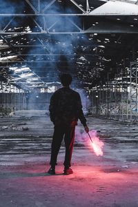 Full length rear view of man holding distress flare in abandoned factory