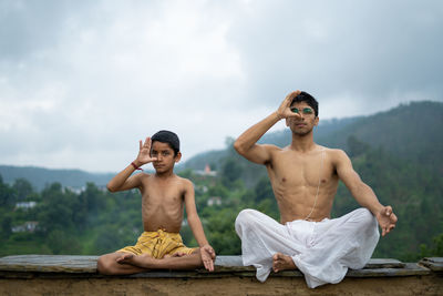 Full length of shirtless boy sitting against sky