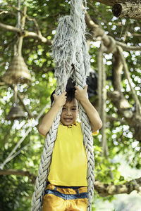 Portrait of boy hanging on rope against trees