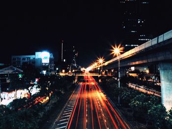 High angle view of light trails on road by bridge in city at night