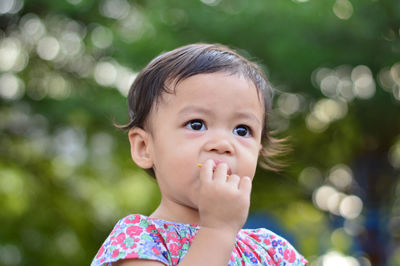 Close-up of cute girl eating while looking away against tree