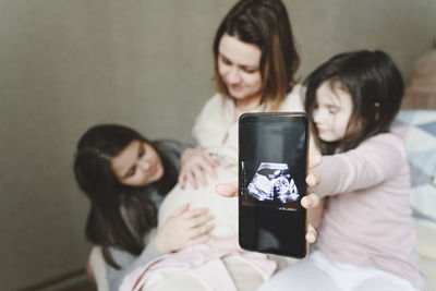 Women holding smart phone while using laptop