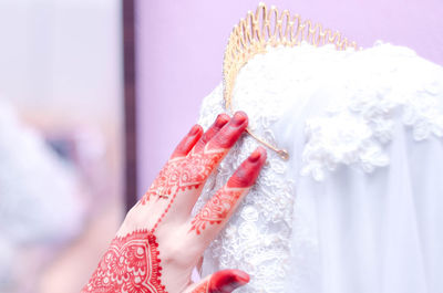 Cropped image of bride with henna tattoo on hand touching crown during wedding