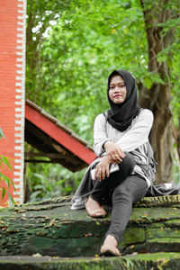 Portrait of smiling young woman sitting against plants