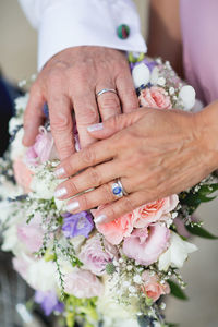 Cropped hands of bride and bridegroom touching bouquet