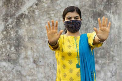 Indian woman in yellow dress showing open palm or stop gesture and looking at camera