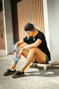 Woman with skateboard sitting in city