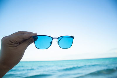 Close-up of human hand holding blue sea against sky