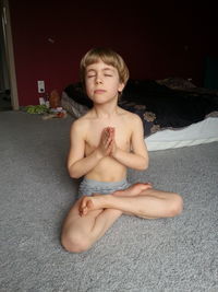 Boy meditating in lotus position on floor at home