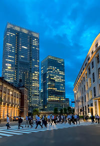 People on street amidst buildings in city against blue sky