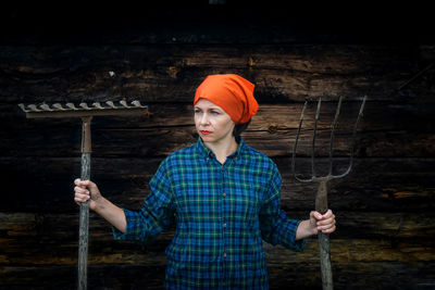 Beautiful woman holding gardening equipment while standing against wooden wall
