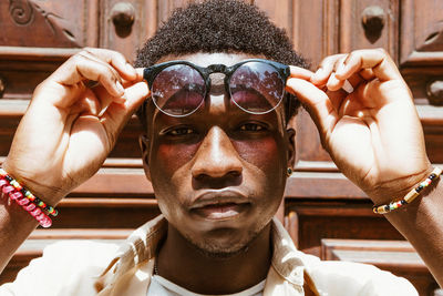 Handsome african american male with afro hairstyle and in stylish sunglasses standing near doors in city and looking at camera