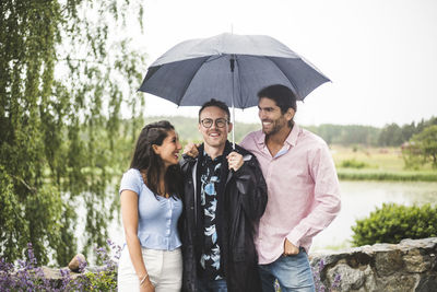 Happy friends standing below umbrella during weekend getaway