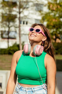 Happy pretty smiling young teen girl wearing bright colorful top and sunglasses with pink headphones