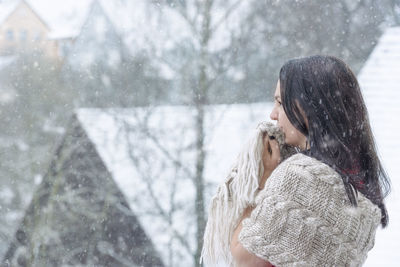 Side view of woman standing against houses during snowfall