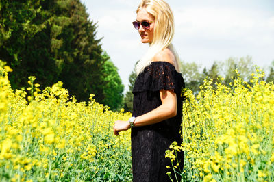 Young woman standing amidst yellow flowers on oilseed rape field