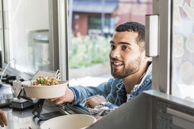 Smiling young male customer holding fresh tex-mex in bowl at concession stand