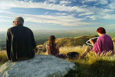 Rear view of people sitting on shore against sky