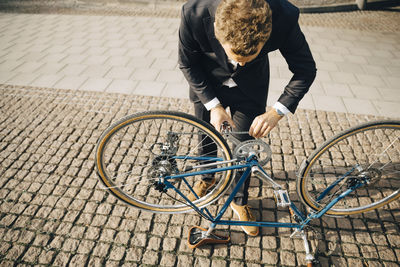 High angle view of businessman repairing bicycle chain on cobbled footpath in city