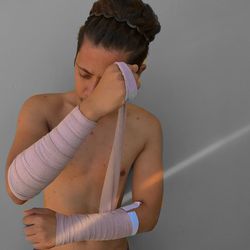 Shirtless young man tying bandage while standing against wall