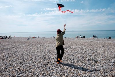 Rear view of friends standing on beach against sky