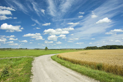 Empty road amidst agricultural field against sky