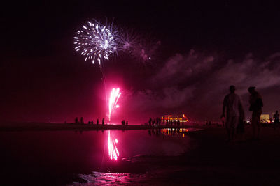 Firework display over sea against sky at night