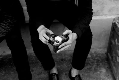 Low section of man holding camera while sitting on retaining wall