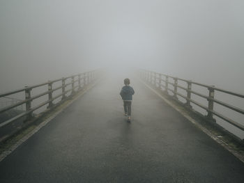 Man on footbridge over sea against sky during foggy weather