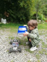 Baby boy crouching while playing with toy car outdoors