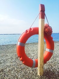 Lifeguard ring hanging from wooden post at beach against sky