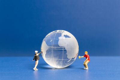 Low angle view of hand holding crystal ball against clear blue sky