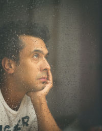 Portrait of woman looking through wet window