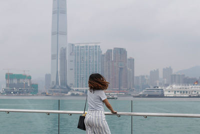 Rear view of woman looking at sea by buildings against sky