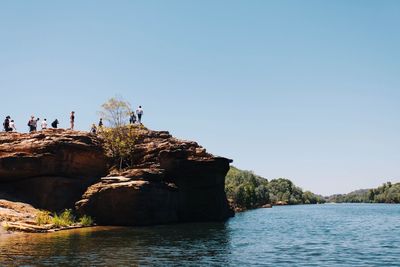 People standing on rock formation by lake against sky